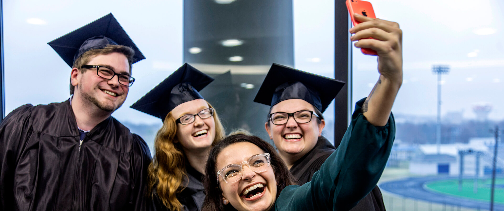 Three graduates and a friend taking a selfie on a cell phone