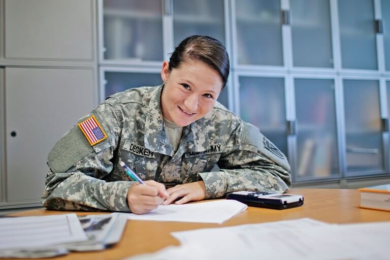 Woman in military uniform smiling at the camera while writing on a paper