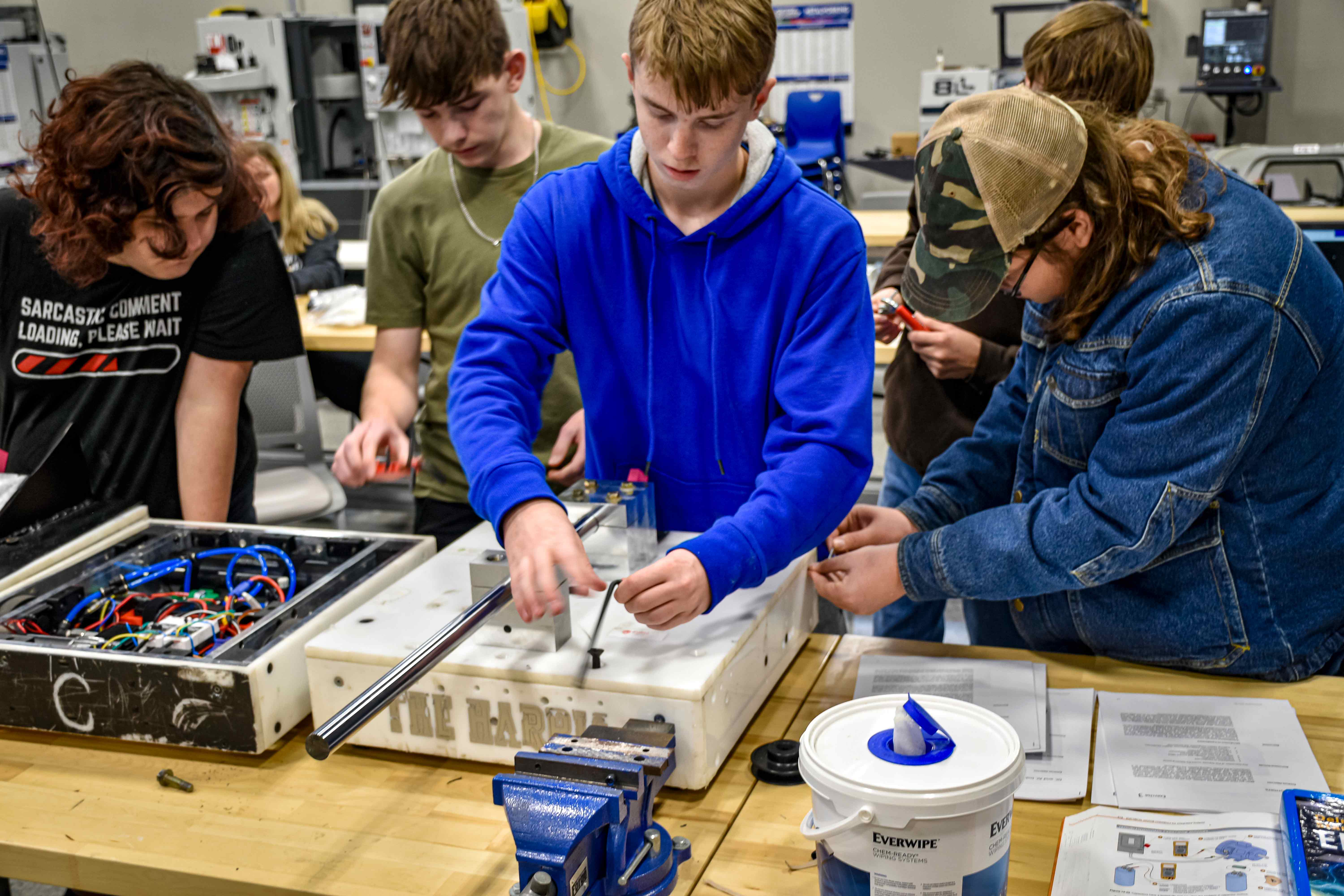 Students collaborating on an engineering project, working with tools and electrical components in a hands-on classroom setting